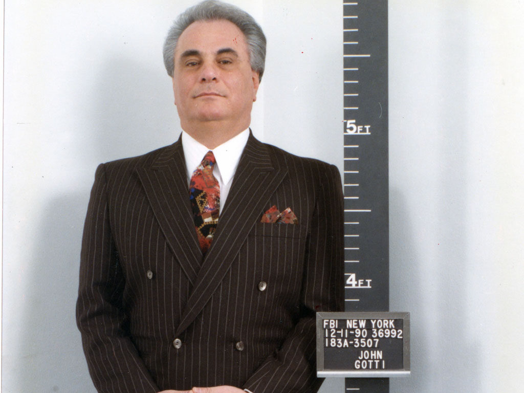 John Gotti in a striped suit beside an FBI New York booking placard dated December 11, 1990.